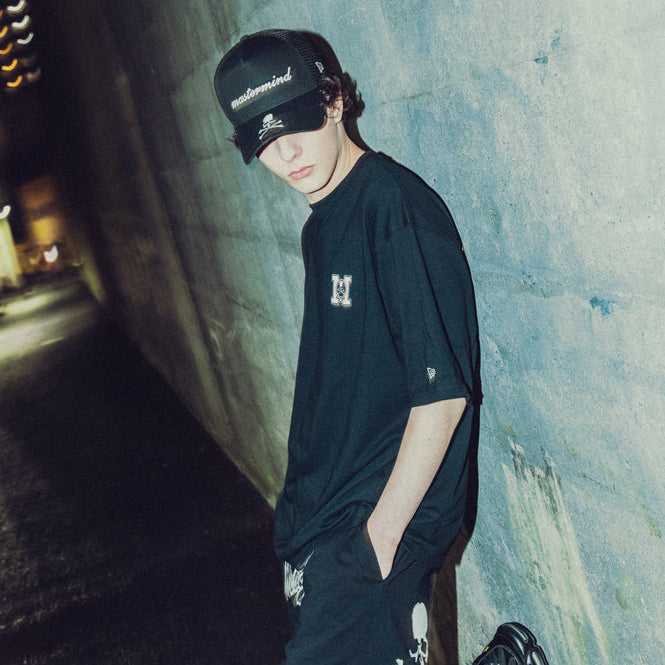 Black Mastermind Japan X New Era trucker cap with embroidered logo, mesh back, and adjustable strap.