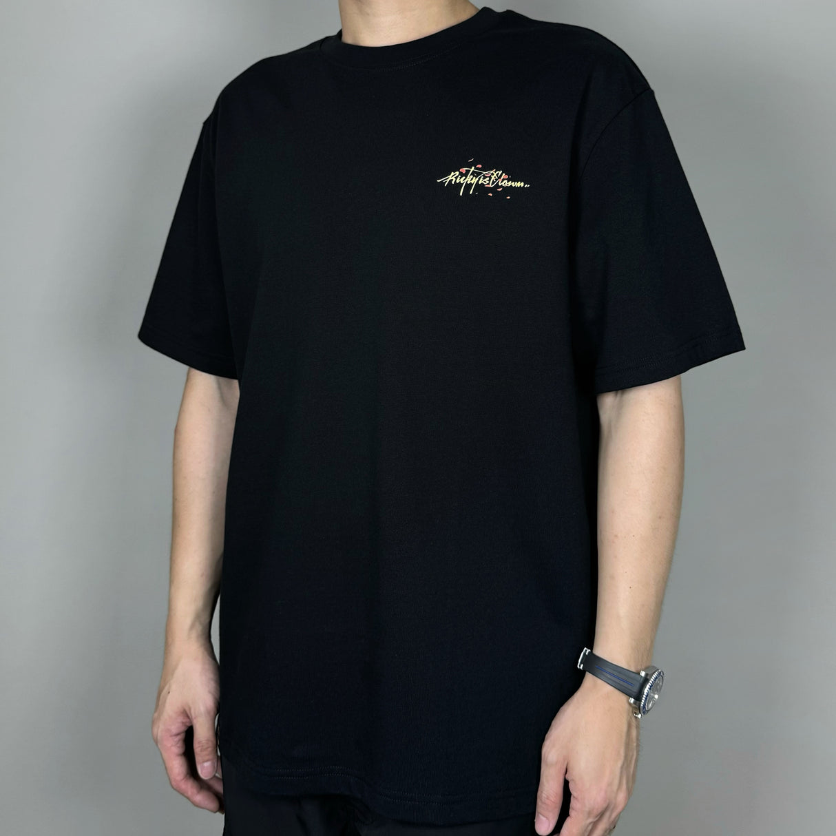 Black Rickyisclown Sakura Sunset Tee displayed on a hanger, showcasing the front design and casual streetwear style.