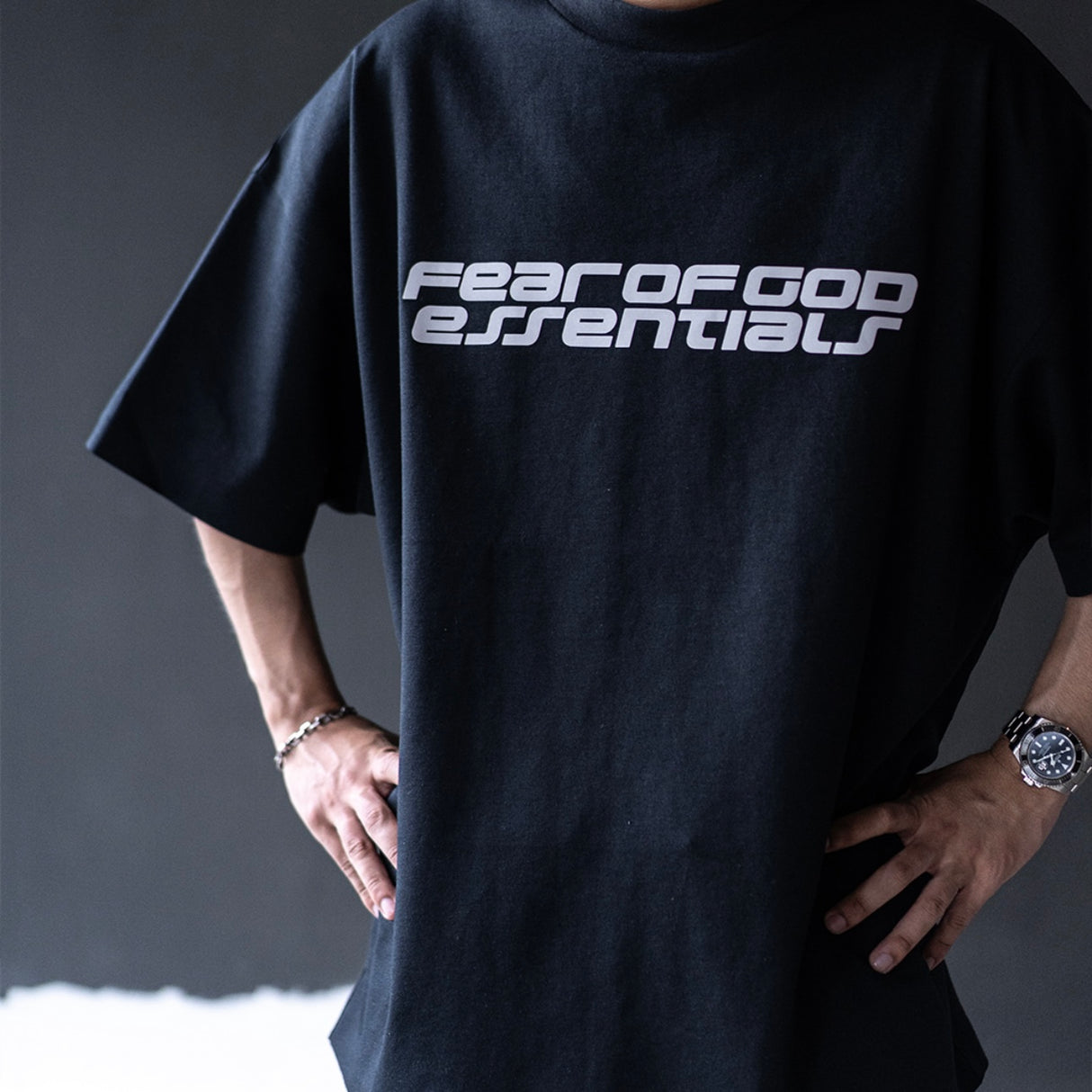 Black Fear of God Essentials Reflective Logo 90s Tee, casual t-shirt with reflective logo print, front view, laid flat.