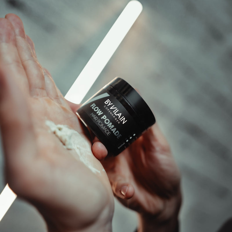 By Vilain Flow Pomade in a jar, showcasing its glossy clay texture and sleek packaging for styling hair with a matte finish.