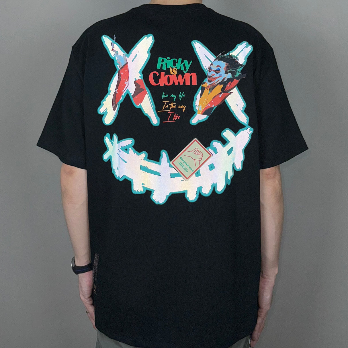 Black Rickyisclown Joker Laser Reflective Smiley T-shirt featuring a bold smiley graphic on the front, casual streetwear style.
