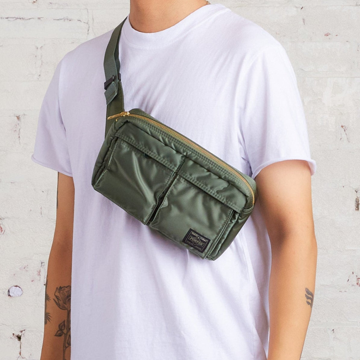 Porter Yoshida Japan Tanker waist bag in sage green with adjustable strap and multiple compartments, styled for casual wear.