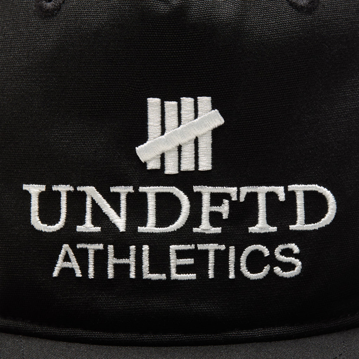 Black Undefeated logo snapback hat, athletic-style headwear with adjustable strap and flat brim, branded by UNDEFEATED.