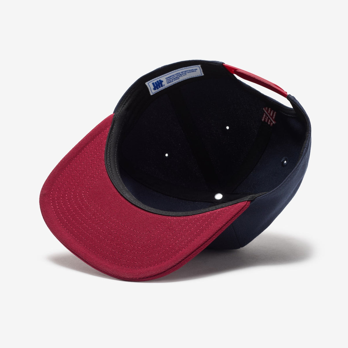 Navy and red Undefeated Play Dirty snapback hat with embroidered logo, casual headwear accessory.