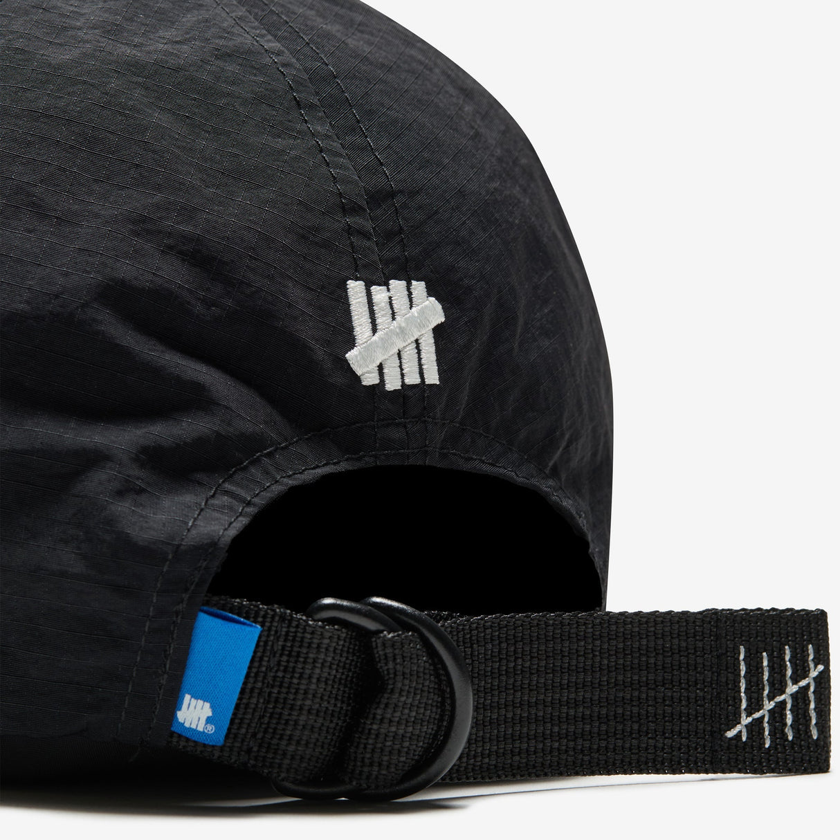 Black Undefeated Logo Strapback headwear with adjustable strap and iconic brand logo on front, view from side angle.