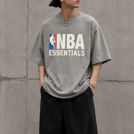 Fear of God Essentials NBA 90s Heavyweight Tee in concrete heather, showing the relaxed fit and classic design on the front.