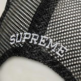 Black Supreme mesh trucker cap with adjustable snapback closure, featuring a classic headwear design and breathable mesh panels.