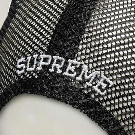 Black Supreme mesh trucker cap with adjustable snapback closure, featuring a classic headwear design and breathable mesh panels.