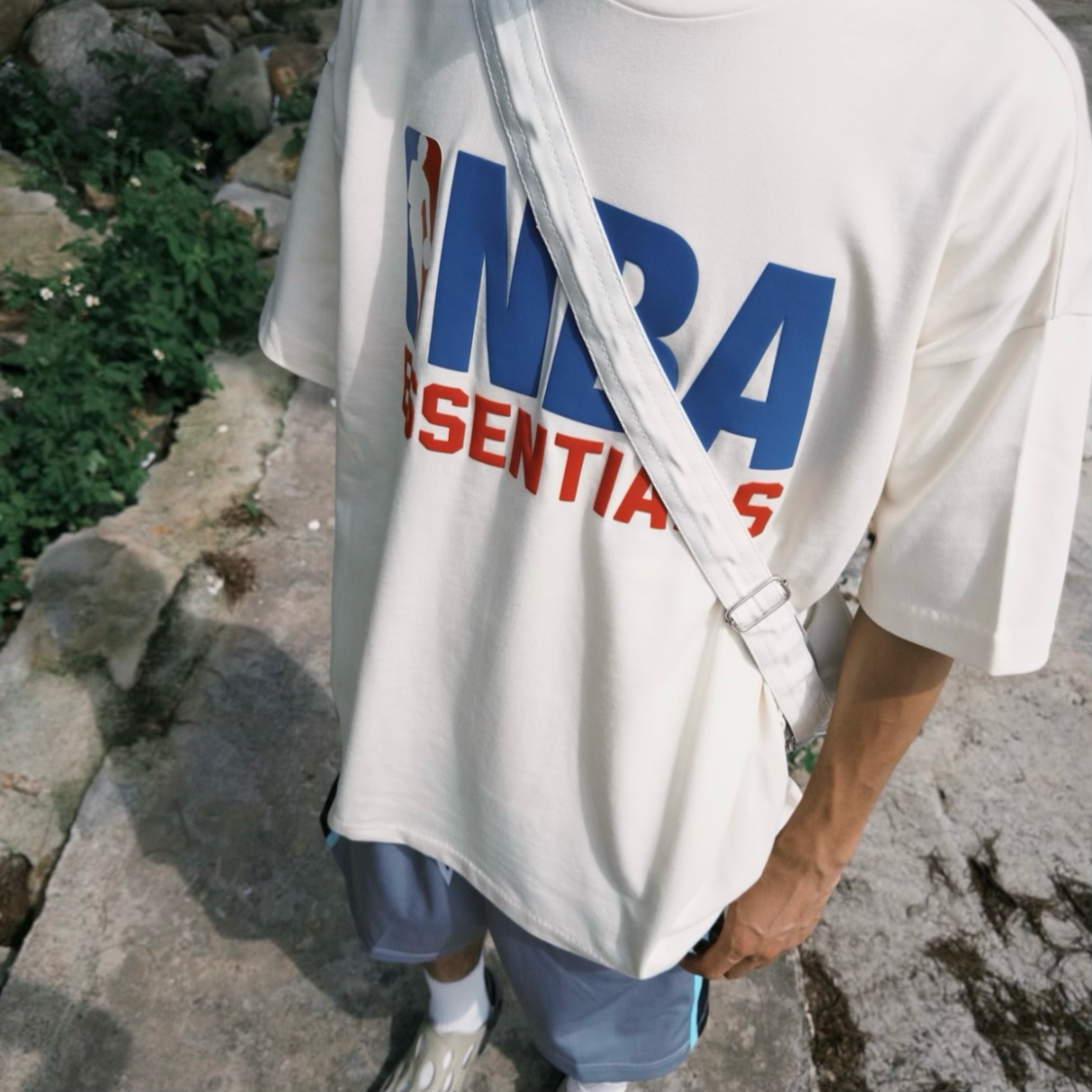 Cream Fear of God Essentials NBA 90s heavyweight tee in apparel, featuring bold graphics and relaxed fit, brand logo visible.