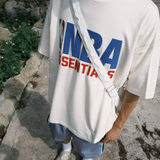 Cream Fear of God Essentials NBA 90s heavyweight tee in apparel, featuring bold graphics and relaxed fit, brand logo visible.
