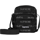 Supreme reflective black shoulder bag with silver monogram logo, featuring a sleek design and adjustable strap.