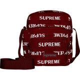 Supreme reflective monogram logo shoulder bag in red with silver logo detail, featuring a compact design and adjustable strap.