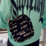 Supreme black shoulder bag with reflective monogram logo, featuring a sleek design and adjustable strap.