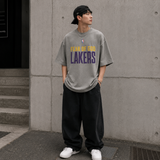 Fear of God Essentials x Lakers NBA 90s heavyweight tee in concrete, featuring bold Lakers logo and vintage-inspired design.