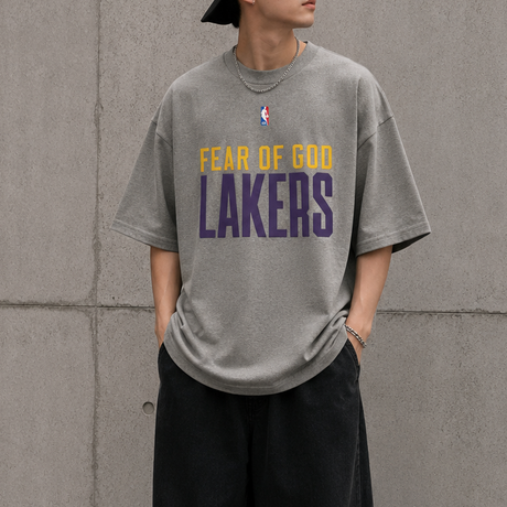 Fear of God Essentials X Lakers NBA heavyweight t-shirt in concrete color, featuring Lakers logo and 90s-inspired design.
