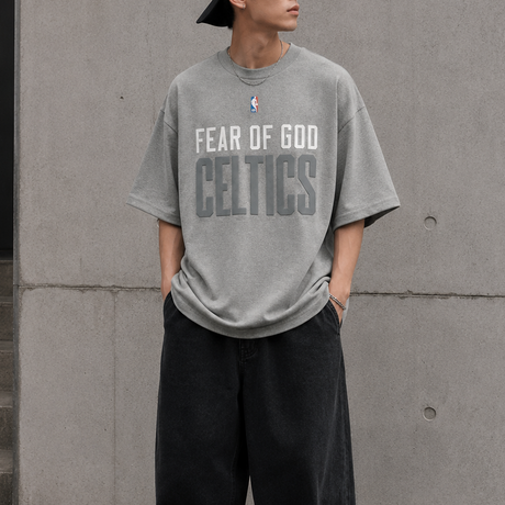 Fear of God Essentials X Celtics NBA heavyweight tee in concrete, showing the front view with team logo and relaxed fit.
