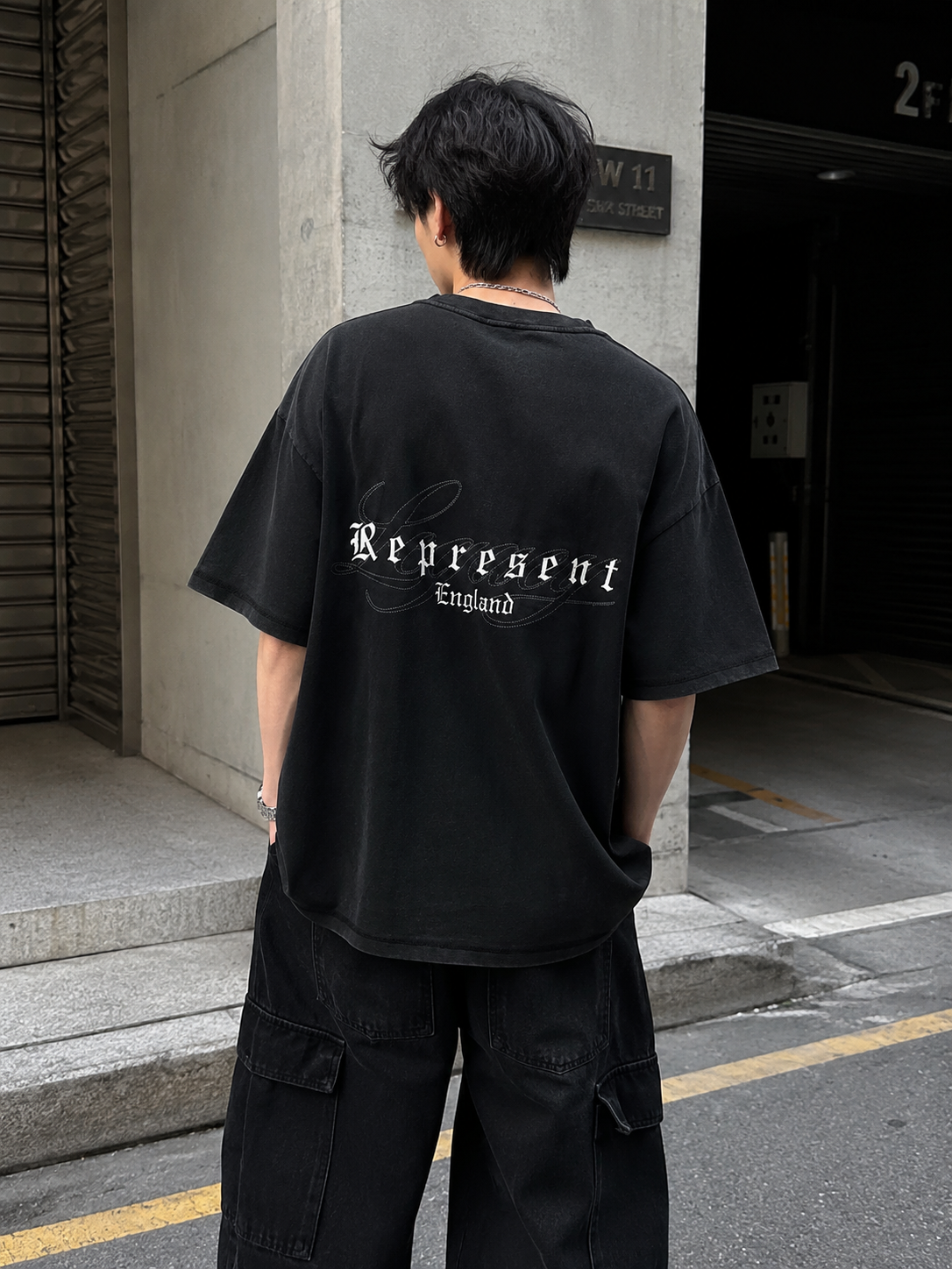 Black Represent Legacy Overprint Tee displayed on a hanger, showcasing the classic design and logo on the front.