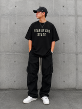 Black Fear of God Essentials 90's Tee displayed on a hanger, showcasing the casual streetwear style and soft cotton fabric.