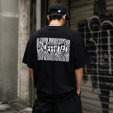 Black Undefeated Trip Logo T-shirt, casual apparel with printed logo, made by UNDEFEATED, shown on a hanger.
