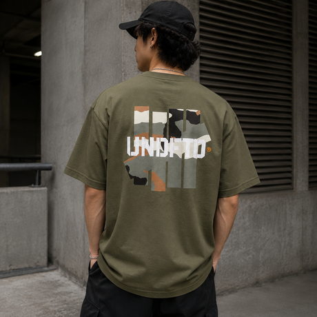 Undefeated Camo Icon Tee in olive green displayed on a hanger, showcasing the camouflage pattern and brand logo.