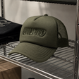 Undefeated Surplus Trucker hat in olive green with mesh back, adjustable strap, and embroidered logo on front.