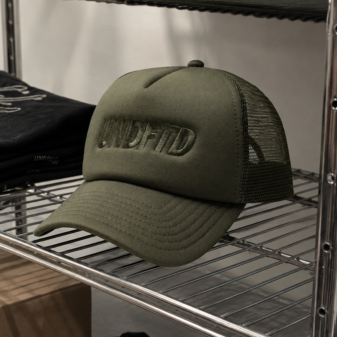 Undefeated Surplus Trucker hat in olive green with mesh back, adjustable strap, and embroidered logo on front.