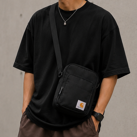 Black Carhartt crossbody zip bag with adjustable strap and front pocket, designed for convenient carrying and everyday use.