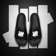 Black Undefeated Signature Logo Slides shoes with bold branding and comfortable slide design, perfect for casual wear.