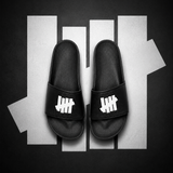 Black Undefeated Signature Logo Slides shoes with bold branding and comfortable slide design, perfect for casual wear.