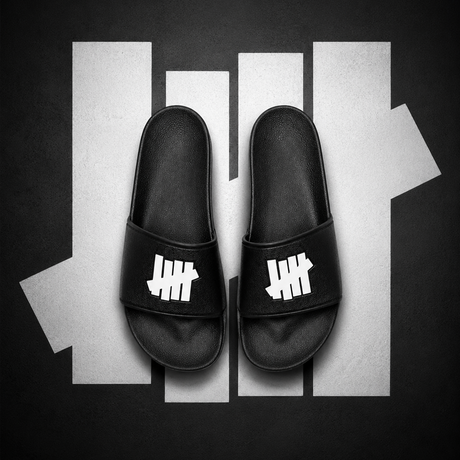 Black Undefeated Signature Logo Slides shoes with bold branding and comfortable slide design, perfect for casual wear.