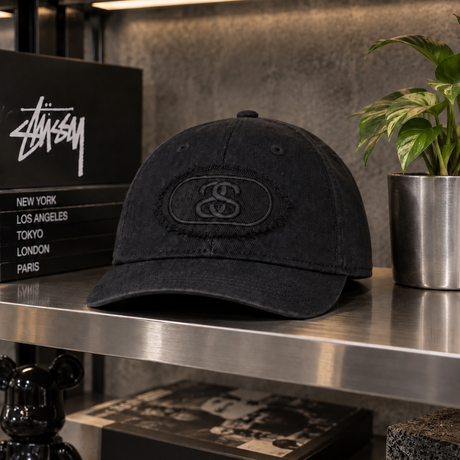 Black Stussy Pill Logo Snapback cap, a stylish headwear accessory featuring the iconic Stussy branding and adjustable snap closure.