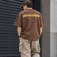 Brown ABOUT:BLANK Box Logo Tee shirt with black logo print on front, casual apparel for everyday wear.