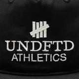 Black Undefeated logo snapback hat, athletic-style headwear with adjustable strap and flat brim, branded by UNDEFEATED.
