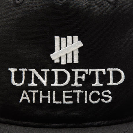 Black Undefeated logo snapback hat, athletic-style headwear with adjustable strap and flat brim, branded by UNDEFEATED.
