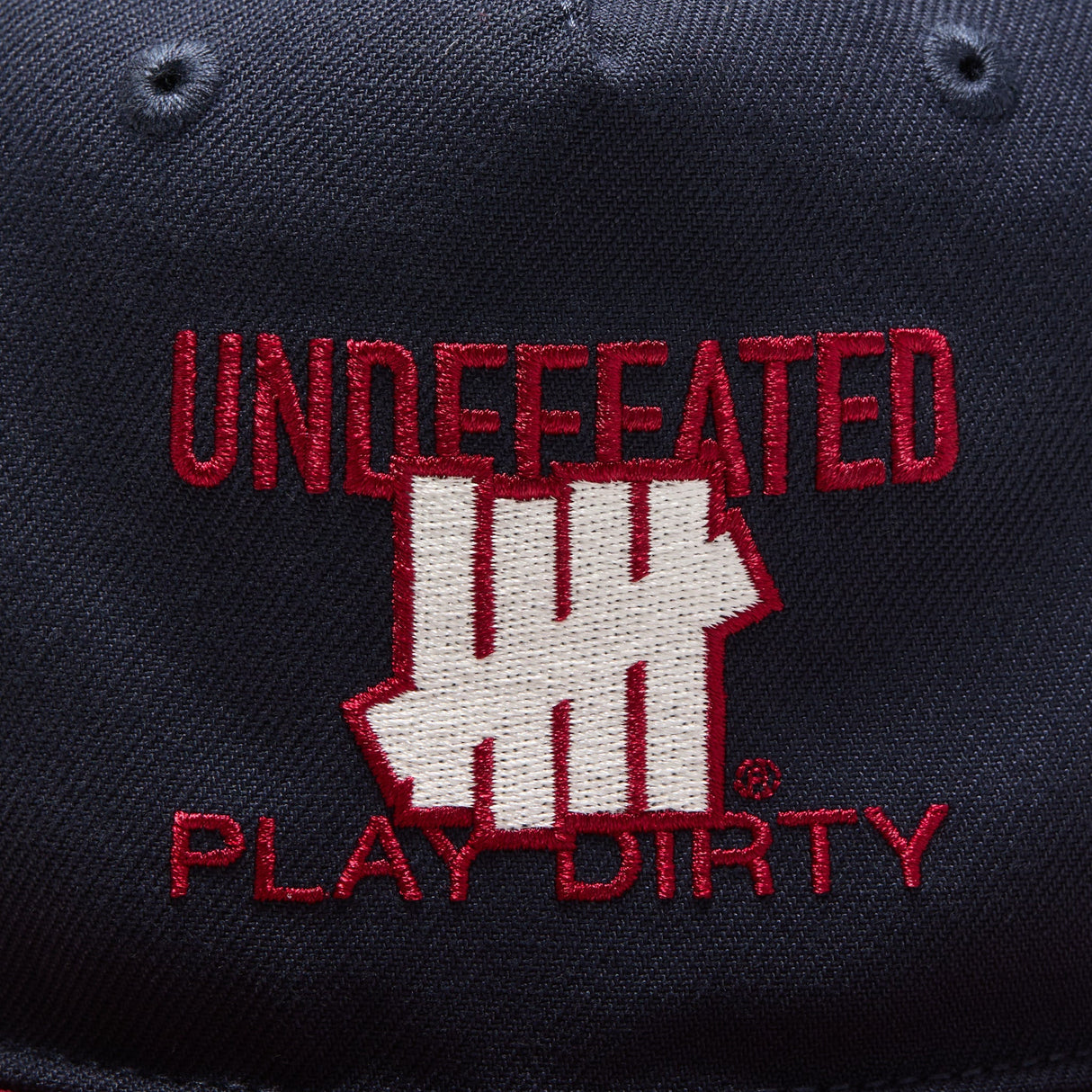 Navy and red Undefeated Play Dirty snapback hat, casual headwear with adjustable strap, featuring embroidered logo details.