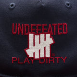 Navy and red Undefeated Play Dirty snapback hat, casual headwear with adjustable strap, featuring embroidered logo details.