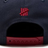 Navy and red Undefeated Play Dirty Snapback hat featuring adjustable snapback closure and embroidered branding.