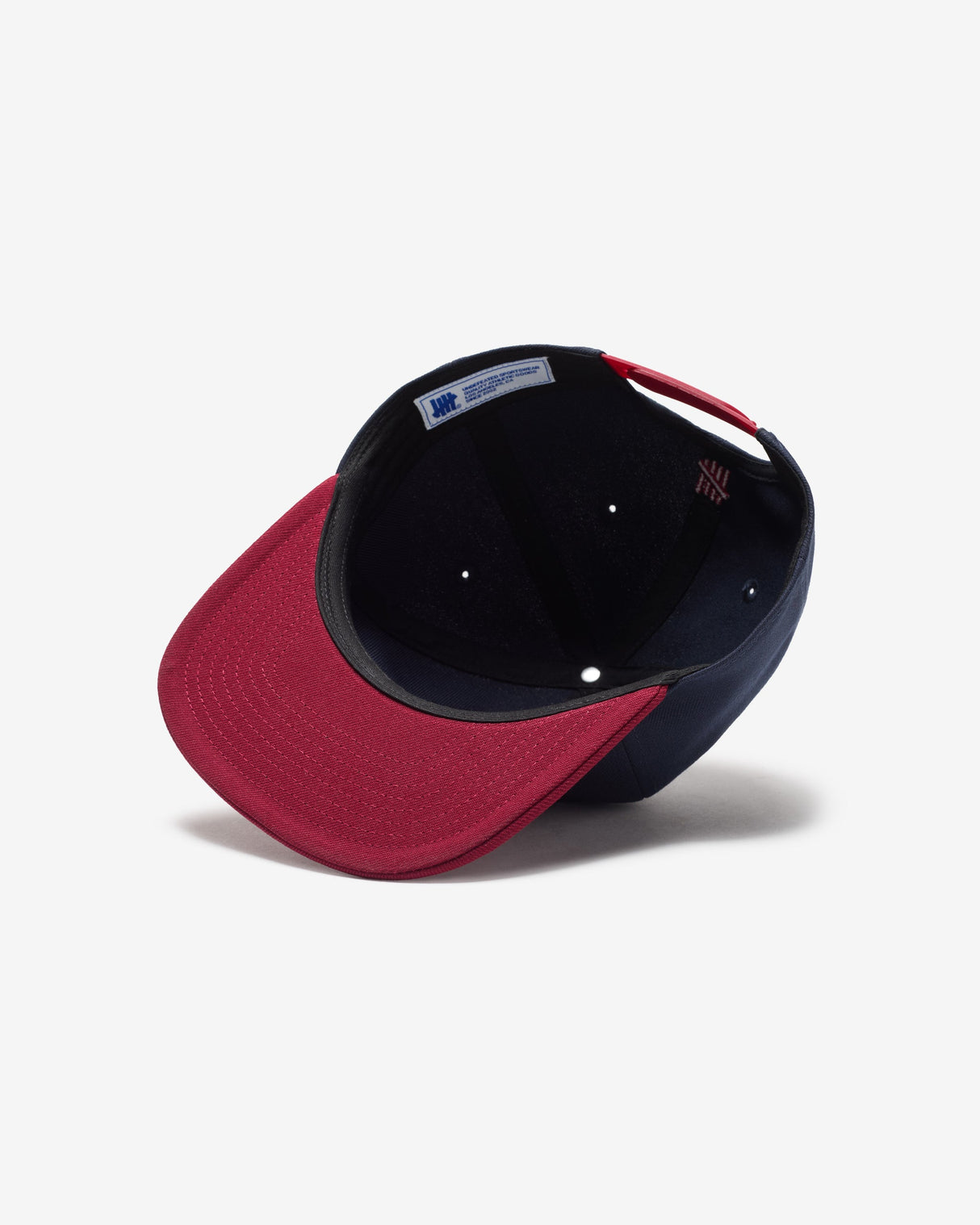 Navy and red Undefeated Play Dirty snapback hat with embroidered logo, casual headwear accessory.