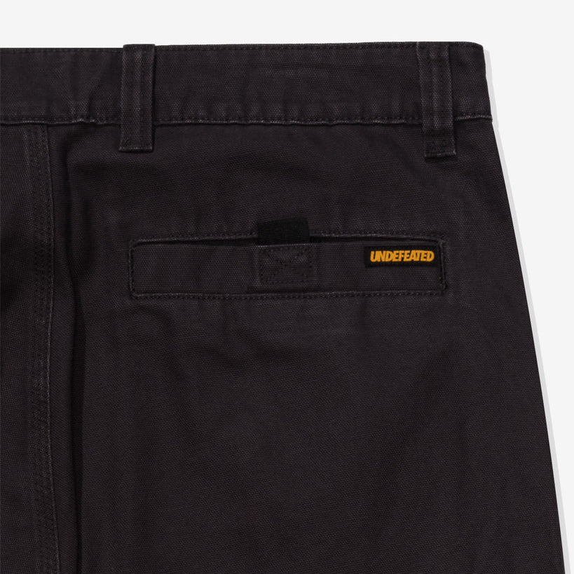 Black Undefeated Utility Pants shown from the side, featuring multiple pockets and a relaxed fit for casual wear.