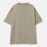 Fear of God Essentials metallic logo classic fit tee in Abbey Stone, showing a casual short-sleeve t-shirt with logo details.