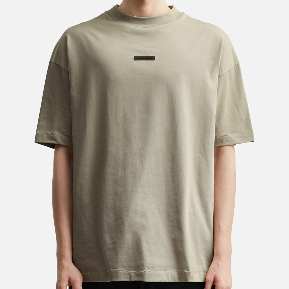 Fear of God Essentials metallic logo classic fit T-shirt in Abbey Stone, showing a close-up of the front with logo detail.